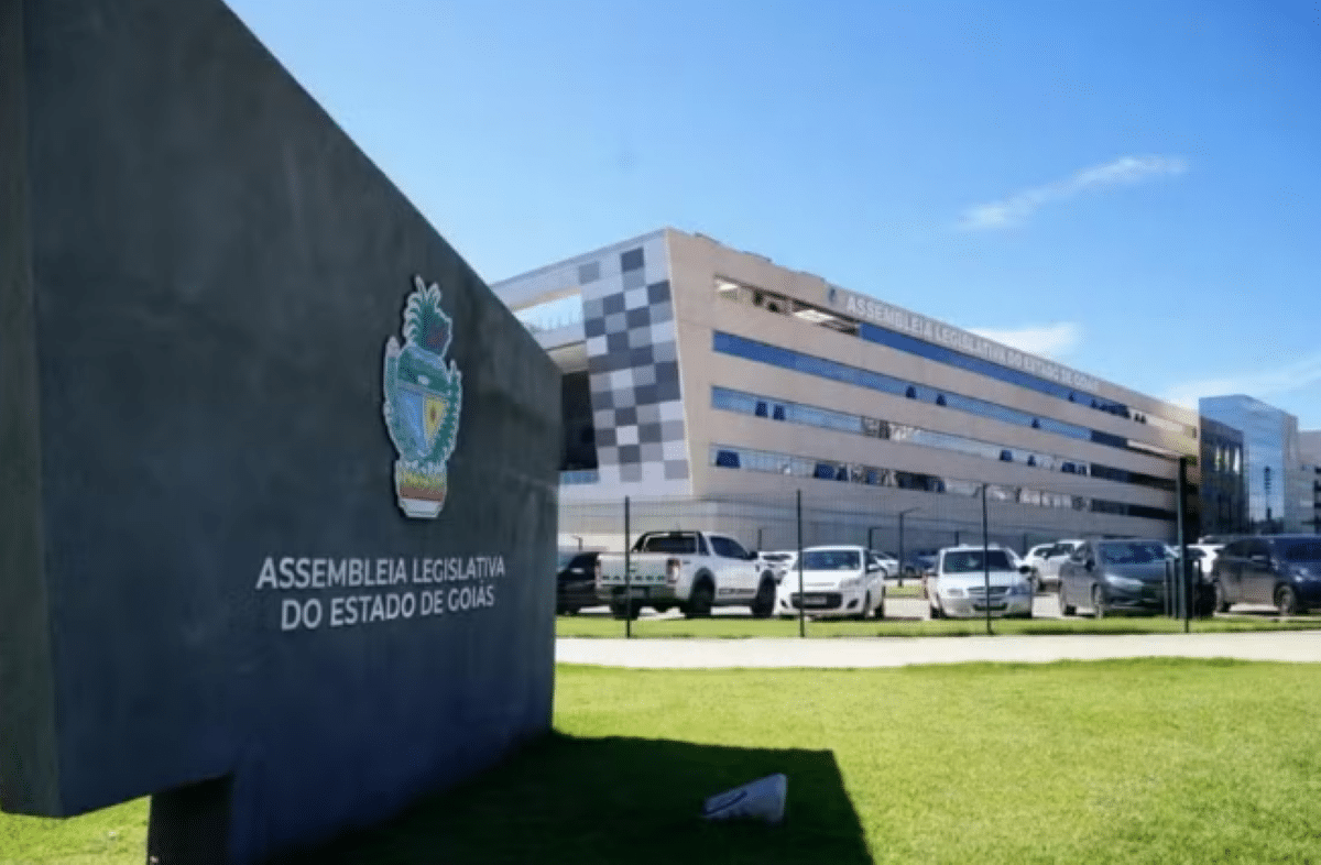 Fachada moderna da Assembleia Legislativa do Estado de Goiás (ALEGO) com estacionamento e céu azul.