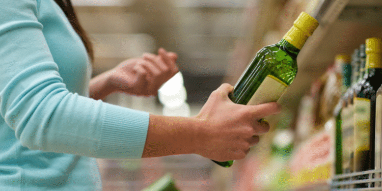 Mulher segurando garrafa de azeite verde enquanto escolhe produto em prateleira de supermercado