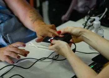 Pessoa com pele morena tendo dedo medido por oxímetro digital segurado por mãos claras