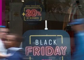 Promoção de Black Friday com 20% de desconto em loja de roupas, com pessoas passando em frente à vitrine.