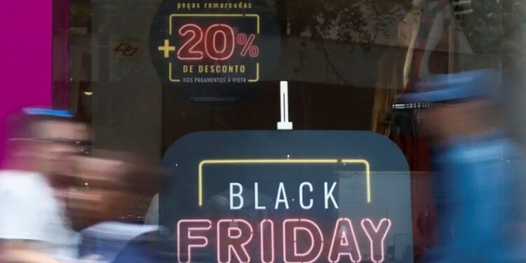 Promoção de Black Friday com 20% de desconto em loja de roupas, com pessoas passando em frente à vitrine.