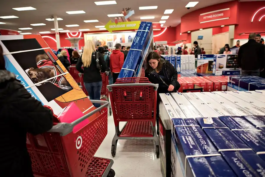 Clientes lotam uma loja de varejo durante a Black Friday, empurrando carrinhos vermelhos cheios de caixas de eletrônicos e eletrodomésticos.