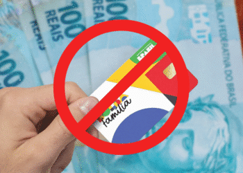 Cartão do Bolsa Família com sinal de bloqueio sobre cédulas de 100 reais. Revisão cadastral e bloqueio de benefício afetam mais de 1 milhão de famílias.