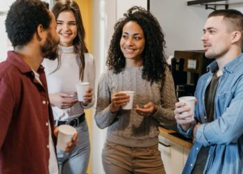 Grupo diversificado de colegas sorrindo e conversando durante uma pausa para café, ilustrando networking informal e conexões profissionais inesperadas.