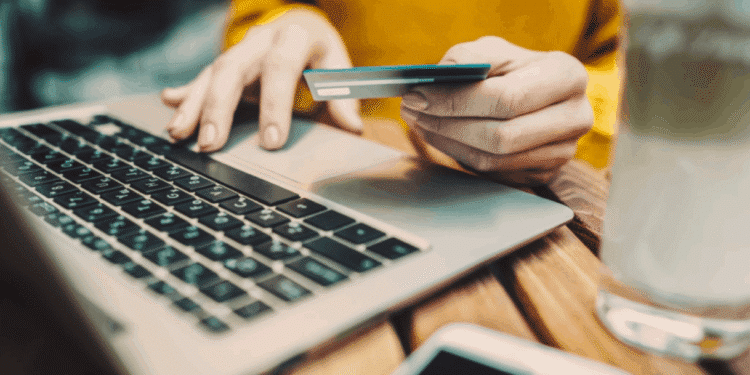 Pessoa realizando compras online com cartão de crédito em seu notebook.