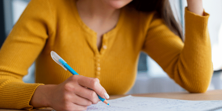 Mulher com blusa amarela escrevendo notas em um caderno aberto com caneta azul.