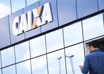 Fachada refletiva da agência da Caixa Econômica Federal com homem ao fundo usando celular