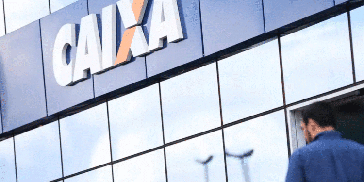 Fachada refletiva da agência da Caixa Econômica Federal com homem ao fundo usando celular
