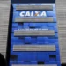 Fachada azul com o logo da Caixa Econômica Federal e frase "A vida pede mais que um banco" em destaque