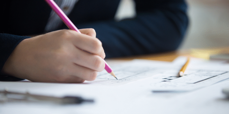 Mão segurando lápis cor de rosa desenhando plantas arquitetônicas sobre mesa com ferramentas de desenho