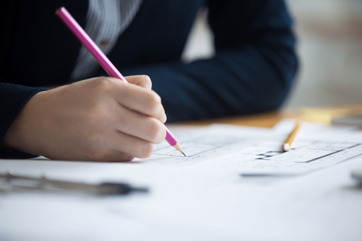 Mão segurando lápis rosa escrevendo ou desenhando em folhas de papel com desenhos e esquemas