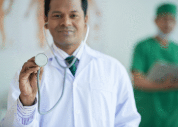 Médico sorridente com jaleco branco e gravata segurando estetoscópio em foco