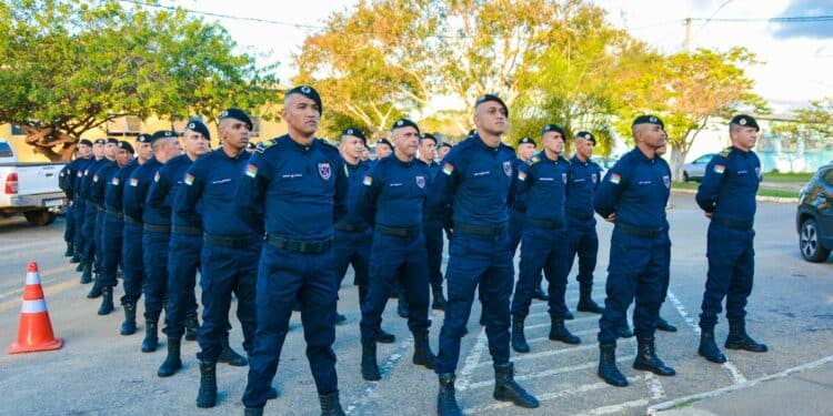 Guardas Municipais fardados em formação alinhada, em área externa com árvores e carros ao fundo.