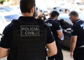 Policiais civis com coletes e uniformes em operação junto a carros estacionados na rua