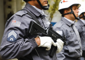 Policiais militares uniformizados em formação segurando armas de fogo com luvas brancas e capacetes