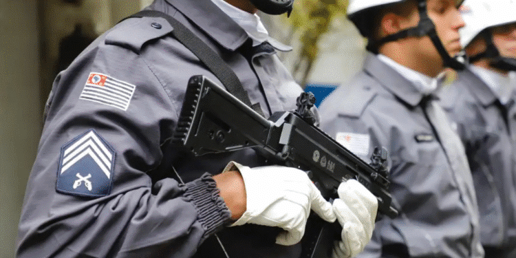 Policiais militares uniformizados em formação segurando armas de fogo com luvas brancas e capacetes