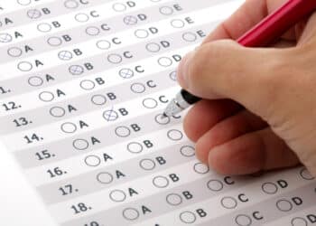 Mão preenchendo resposta de questão de prova de múltipla escolha com caneta vermelha