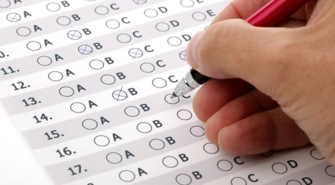 Mão preenchendo resposta de questão de prova de múltipla escolha com caneta vermelha