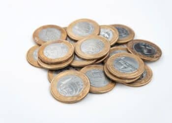 Pilha de moedas brasileiras de R$ 1 em um fundo branco, algumas com sinais de desgaste. Ilustra a matéria sobre moedas raras de R$ 1 que podem valer uma fortuna devido a erros de cunhagem.