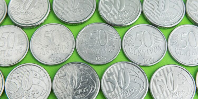 Close-up de diversas moedas brasileiras de 50 centavos, algumas com datas como 1994, 1995 e 2008, procuradas por colecionadores de moedas raras.