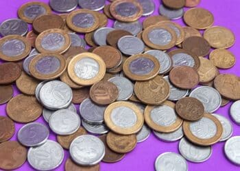 Coleção de moedas brasileiras de diferentes valores e anos, espalhadas sobre um fundo roxo, ilustrando a busca por moedas raras e valiosas.