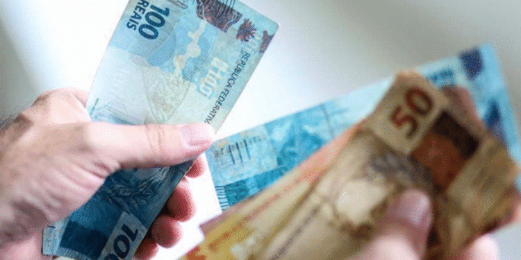 Mão segurando notas de 100 e 50 reais brasileiras, ilustrando pagamento em dinheiro.