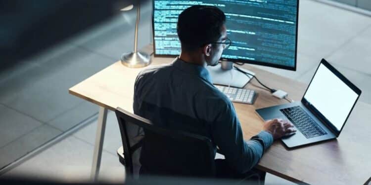 Desenvolvedor ou analista de sistemas trabalhando à noite em frente a um computador, com a tela principal exibindo linhas de código, simbolizando o foco em tecnologia e futuro do trabalho digital.