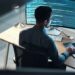 Desenvolvedor ou analista de sistemas trabalhando à noite em frente a um computador, com a tela principal exibindo linhas de código, simbolizando o foco em tecnologia e futuro do trabalho digital.
