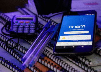 Celular com a tela do aplicativo do Enem aberta ao lado de cadernos, canetas e uma calculadora.