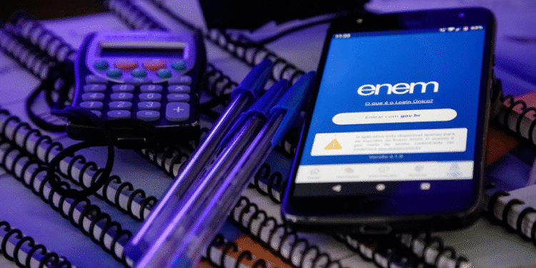 Celular com a tela do aplicativo do Enem aberta ao lado de cadernos, canetas e uma calculadora.