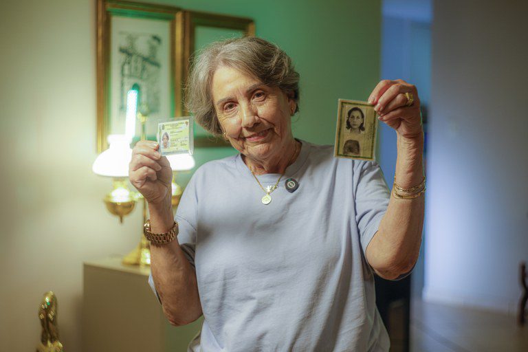 Idosa com 60 anos ou mais mostra a evolução da Carteira de Identidade Nacional (CIN) Senhora idosa sorridente exibe a nova Carteira de Identidade Nacional (CIN) e uma identidade antiga (RG)