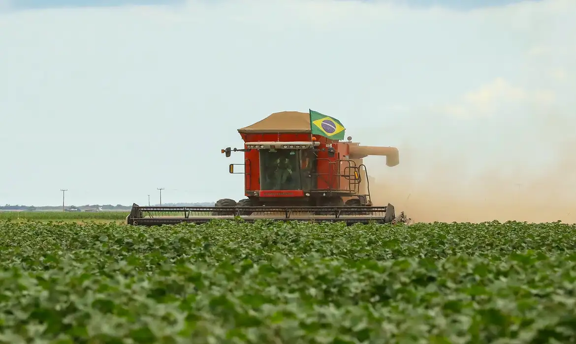 Colheitadeira moderna com a bandeira do Brasil operando em uma lavoura verde, simbolizando a tecnologia avançada e a produtividade no agronegócio brasileiro.