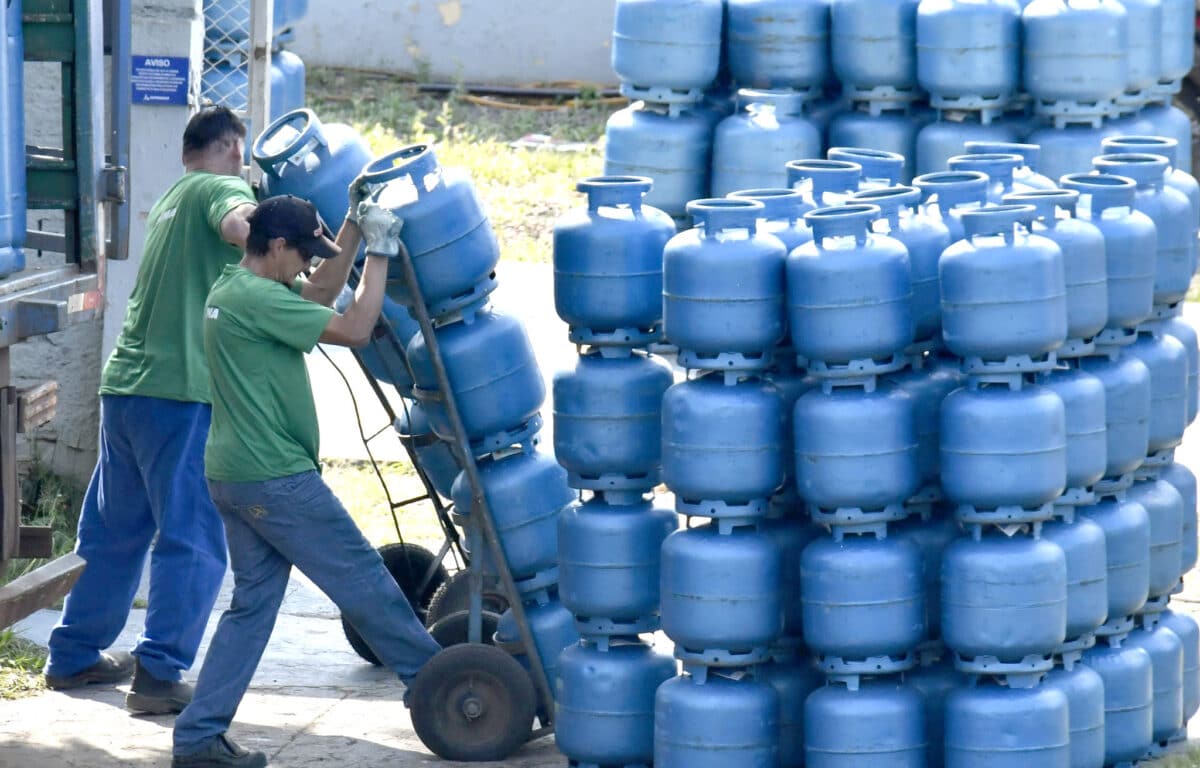 Trabalhadores organizando botijões de gás azul empilhados em área externa
