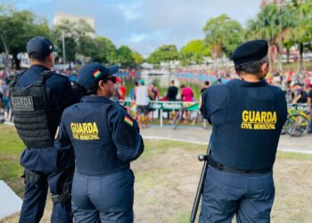 rês agentes da Guarda Civil Municipal em uniforme azul vigiando evento ao ar livre em parque com muitas pessoas