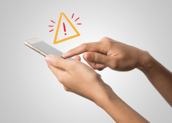 Mãos segurando smartphone com símbolo de alerta próximo à tela cinza