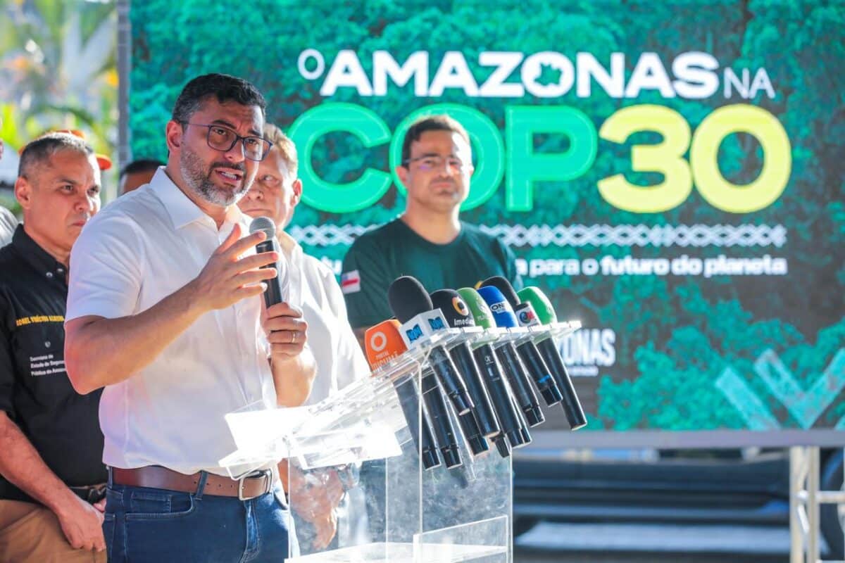 Homem falando em microfone em evento da COP30 com tela ao fundo destacando "Amazonas na COP30".