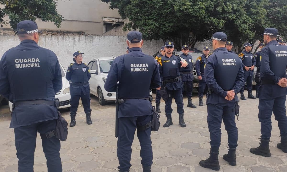 Grupo de guardas municipais em formação vestindo uniformes azuis escuros em pátio externo durante treinamento