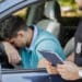 Um policial de trânsito com um clipboard abordando um motorista que parece aflito ao volante, representando as infrações de trânsito e suas penalidades segundo o CTB.