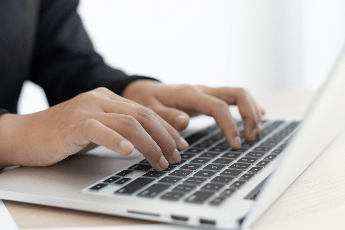 Mãos femininas digitando em teclado de laptop prateado sobre mesa clara