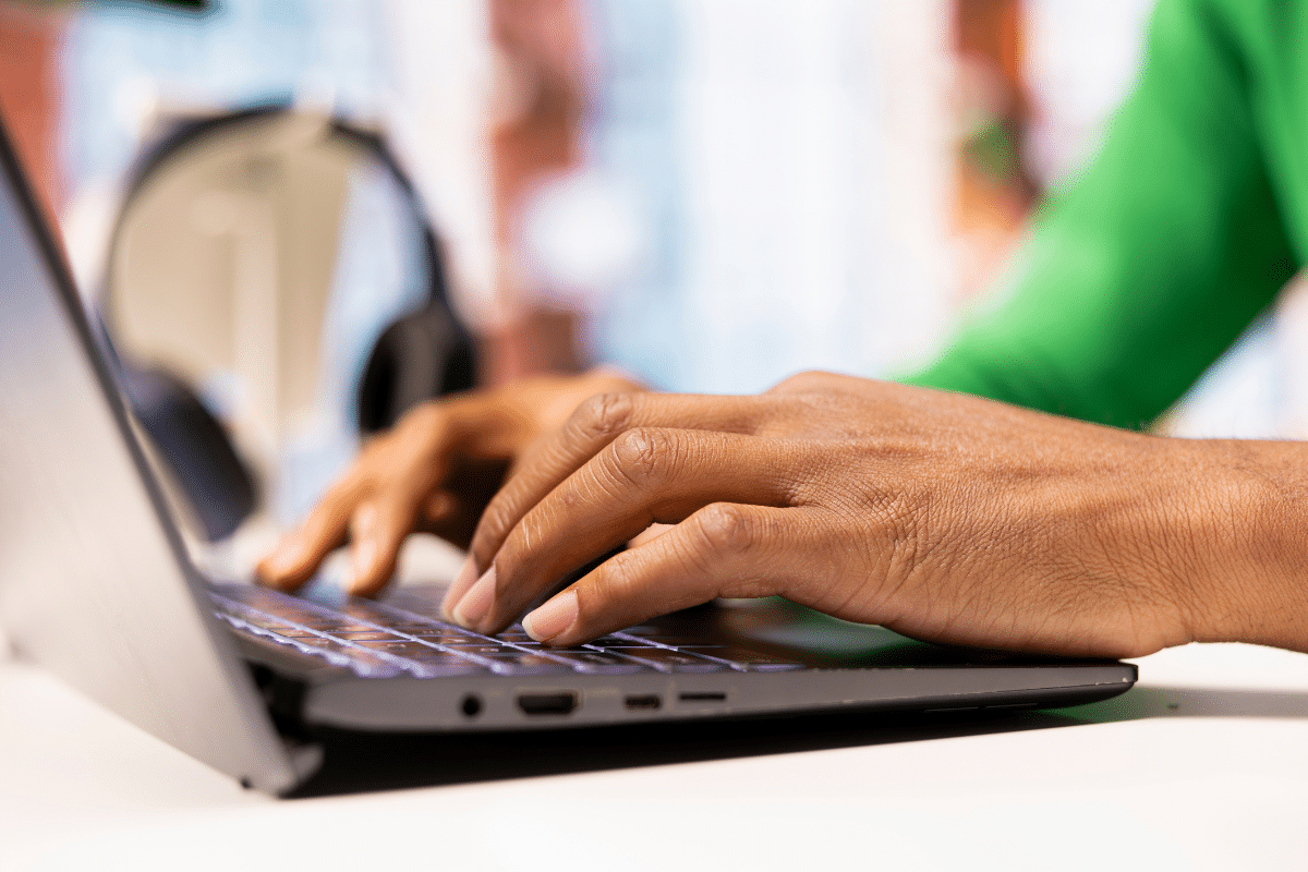 Mãos de pessoa digitando em teclado de notebook preto com vestimenta verde e ambiente claro