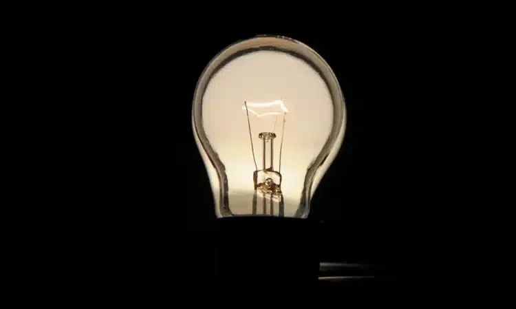 luz tarifa social 750x449 Lâmpada incandescente acesa com fundo preto destacando detalhes internos