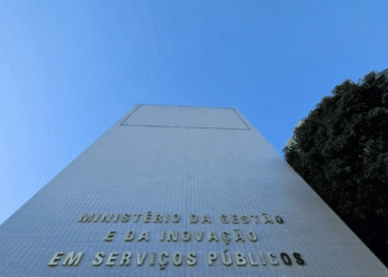 Foto da fachada de um edifício alto com a inscrição "MINISTÉRIO DA GESTÃO E DA INOVAÇÃO EM SERVIÇOS PÚBLICOS" contra um céu azul claro e árvores ao lado.