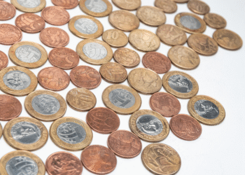 Diversas moedas brasileiras de diferentes valores e cores espalhadas sobre superfície branca