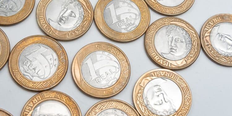 Conjunto de moedas brasileiras de 1 Real espalhadas sobre uma superfície branca, representando colecionismo, valor e numismática.