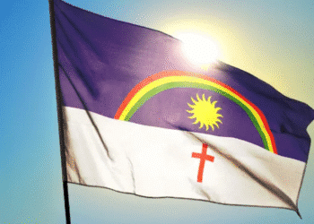 Bandeira do estado de Pernambuco tremulando ao sol, com arco-íris, sol e cruz vermelha.