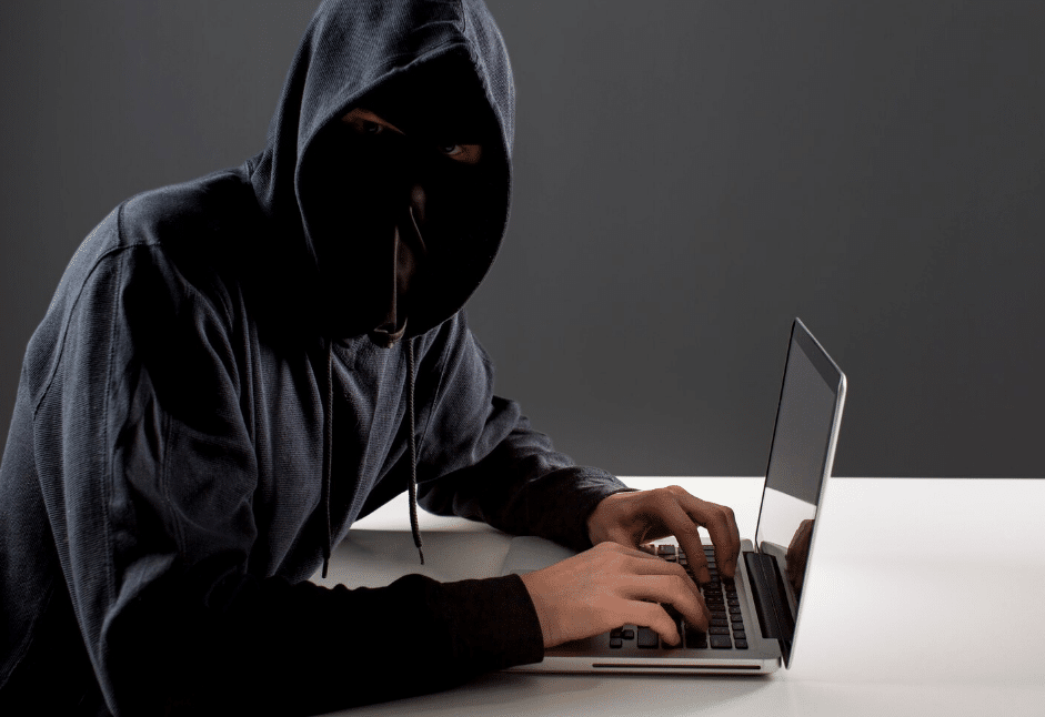 Criminoso digital usando laptop em ambiente escuro, representando golpes noturnos durante a Black Friday.