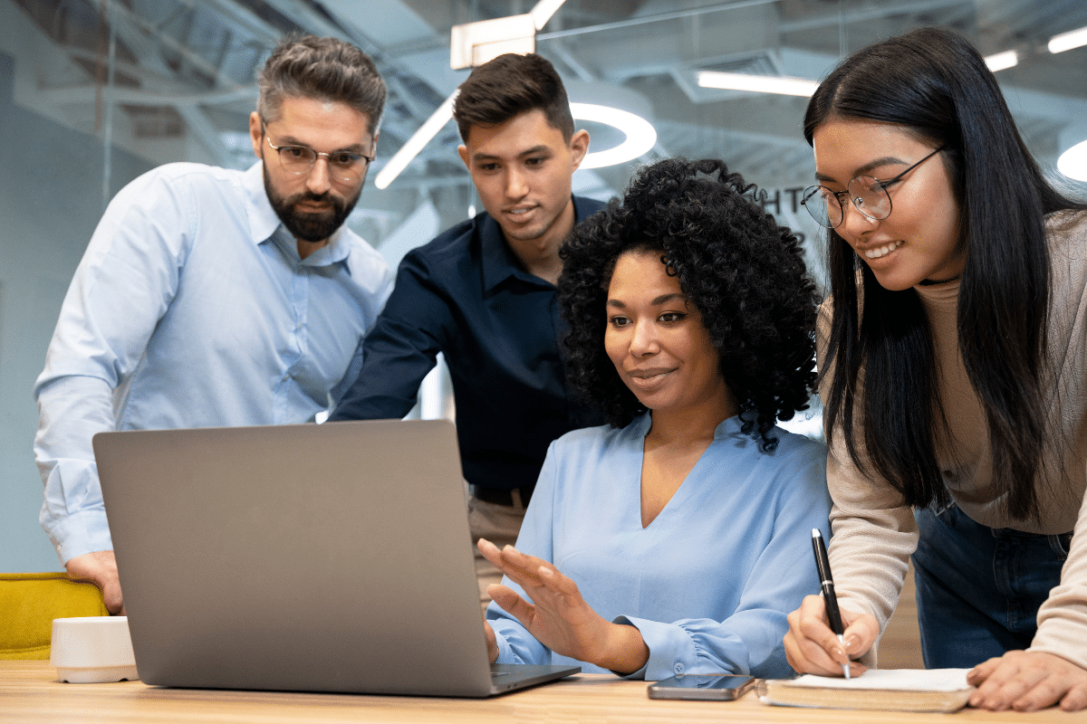 Quatro profissionais jovens colaborando em frente a um notebook em ambiente de escritório moderno