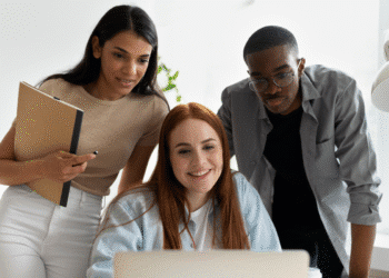 Três jovens profissionais observando e discutindo informações em um laptop durante reunião no escritório