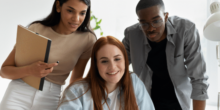 Três jovens profissionais observando e discutindo informações em um laptop durante reunião no escritório