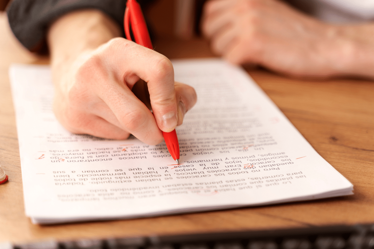 Concursos abertos Mão segurando caneta vermelha revisando texto impresso com anotações e correções em vermelho